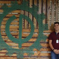 Coordenador Everton Almeida frente a arte fixada no bloco do curso com a engrenagem símbolo da Engenharia Florestal 